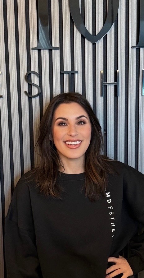 Allison Braverman, team member at MD Esthetics, standing in front of the MD Esthetics logo