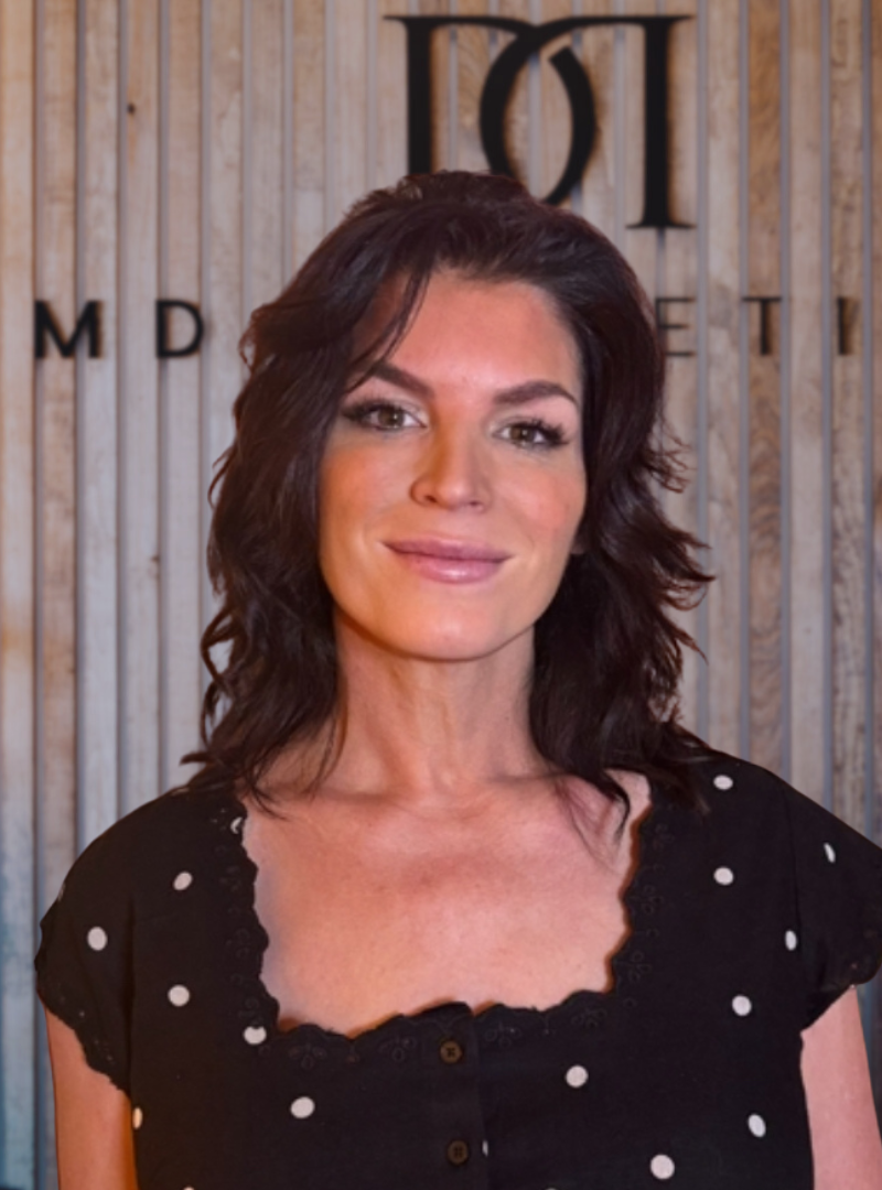 Jannine, team member at MD Esthetics Pittsfield, posing in front of the MD Esthetics logo.