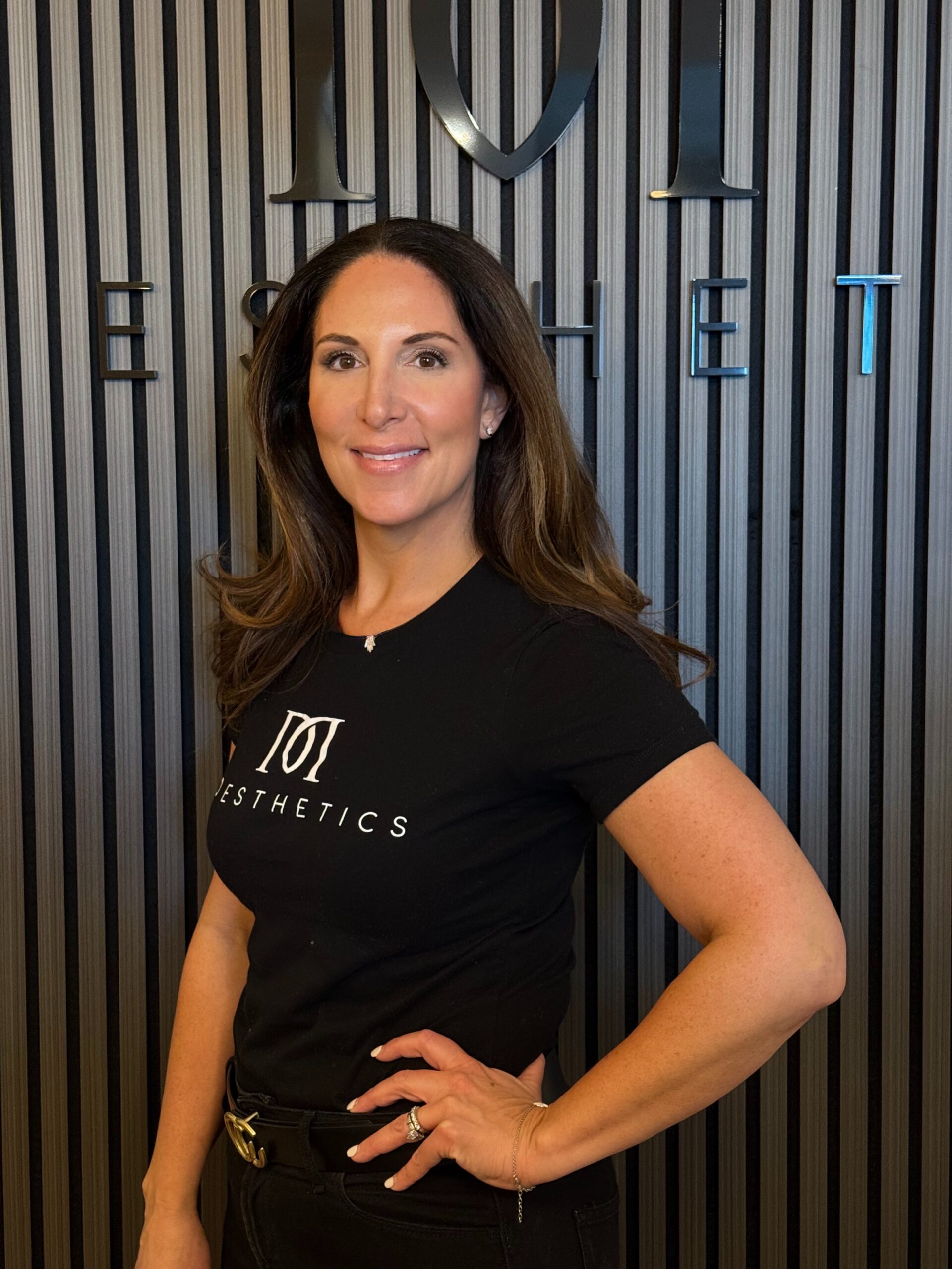 Jennifer Dale, staff member at MD Esthetics, posing in front of the MD Esthetics logo.