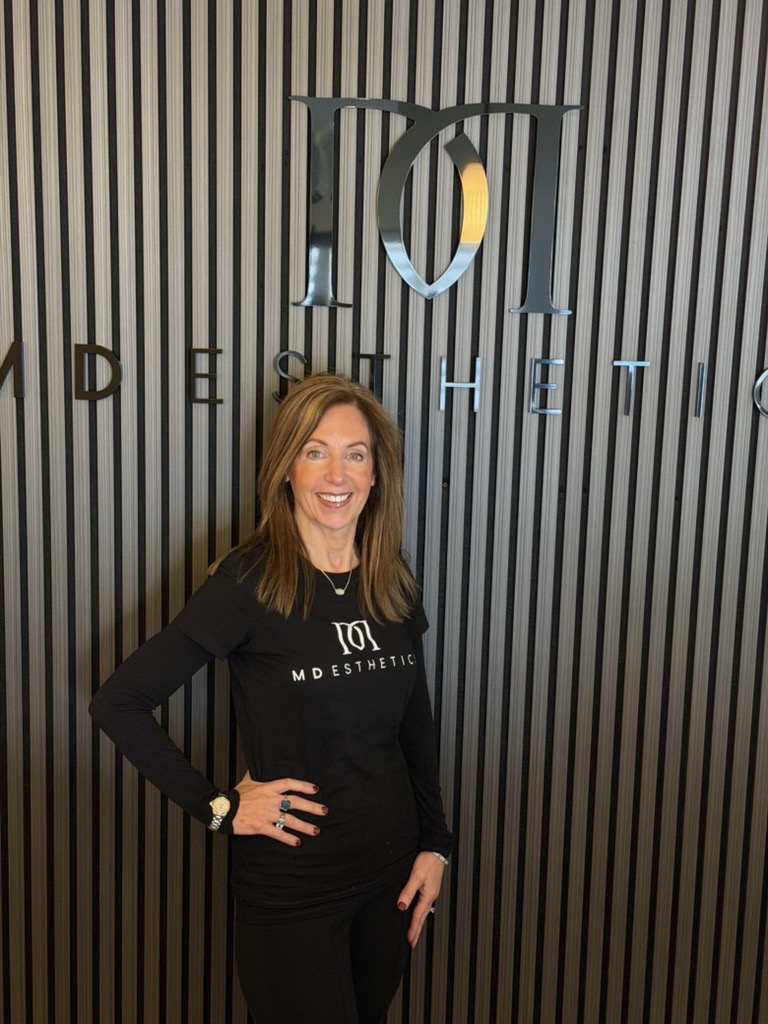 Lisa, staff member at MD Esthetics, posing in front of the MD Esthetics logo.